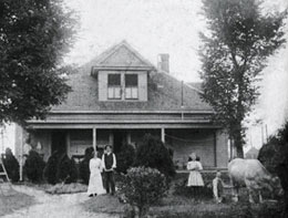 A couple and a young girl with a cow stand in the front yard of a house