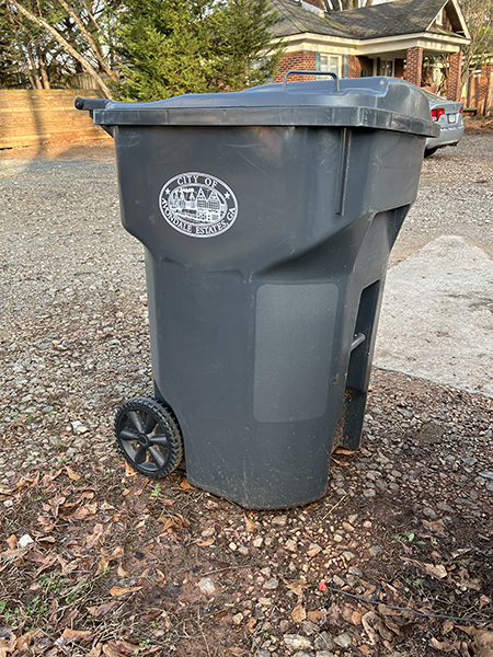 Grey trash receptacle with Avondale Estates city logo in front of house