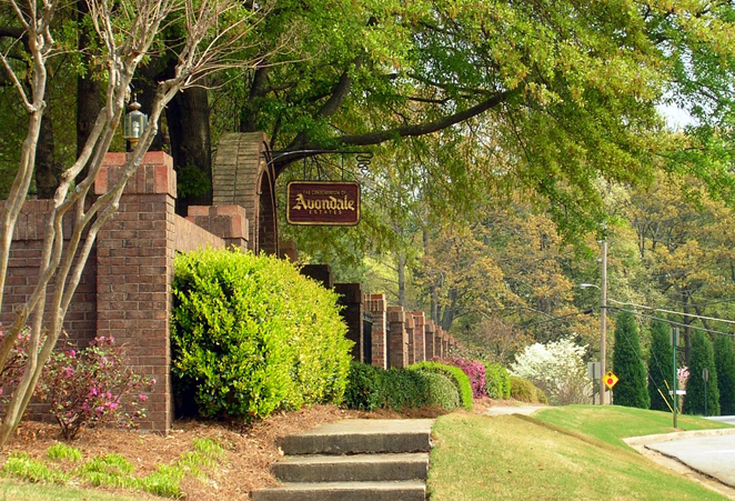 View of a sidewalk with shrubbery, brick fencing, and an Avondale Estates sign